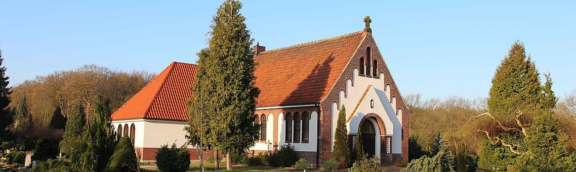 Bild der Friedhofskapelle. Aufgenommen an einem sonnigen Tag. Das ganze Gebäude wird in einem Winkel von ca. 45 Grad zum Eingang abgebildet.